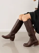 Bota de caña alta confeccionada en cuero vacuno color marrón, con diseño de paneles combinados, cierre lateral y taco cuadrado bajo.