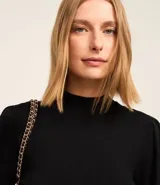 Suéter negro de punto con cuello alto, mangas largas abullonadas y puños largos.