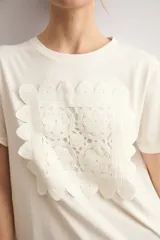 Remera color natural de manga corta, con cuello redondo y un aplique cuadrado de crochet con diseño floral en el centro del pecho.