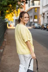 Blusa de algodón color amarillo pastel, con escote redondo ajustable mediante lazo, mangas cortas abullonadas con volados y diseño con textura delicada y terminaciones festoneadas.