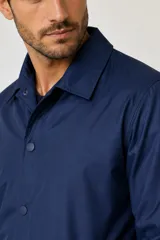 Campera estilo coach de poliéster color azul, con cuello camisero, cierre frontal con botones a presión y bolsillos laterales.