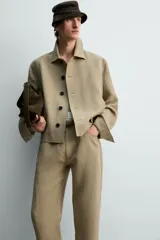 Sobrecamisa cropped fit de lino color beige, con cuello solapa, mangas largas con puño abotonado, bolsillos frontales de vivo y cierre frontal con botones oscuros.