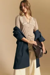 Top tejido de manga corta color beige, con escote en V y cierre frontal de botones. Presenta un cuello amplio con borde en contraste de color blanco.