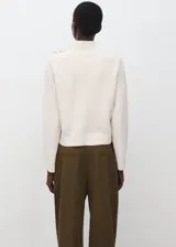 Jersey de punto medio color blanco, con cuello perkins y detalle de botones metálicos en el hombro izquierdo.