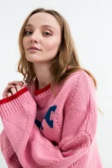 Sweater de punto color rosado con diseño jacquard de peces azules en el pecho, cuello redondo, puños y ruedo en tono rojo contrastante. Presenta textura en rombos y mangas largas holgadas.