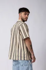 Camisa de manga corta tejida al crochet con diseño de rayas verticales negras sobre una base color crudo. Presenta cuello solapa y cierre frontal con botones.