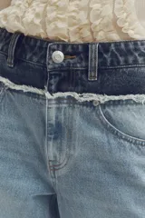 Jean de corte holgado y pierna recta confeccionado en denim de algodón rígido. Presenta un diseño bicolor con paneles en tonos contrastantes, costura desflecada en la cintura y franjas laterales. Cuenta con diseño de cinco bolsillos, cierre con botón y tachas metálicas con logo grabado.