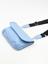 Bolso bandolera de color celeste con solapa frontal, confeccionado en material sintético liso. Incluye una correa ajustable de cinta negra con detalles en cuero sintético celeste y herrajes metálicos plateados.