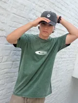 Remera de manga corta color verde oscuro con efecto acid wash y un logo ovalado blanco con el texto "OSTEN" en el centro del pecho.