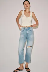Jeans de tiro medio y corte bootcut cropped de Zara Woman Collection. Confeccionados en denim de efecto lavado en color celeste, presentan diseño de cinco bolsillos, trabillas para cinto, detalle de rotura en la rodilla izquierda y bajo evasé sin costuras. Cierre frontal con cremallera y botón metálico.