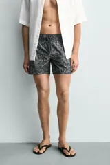 Bañador de hombre de tejido técnico, color gris oscuro con estampado abstracto en tonos más claros. Presenta cintura elástica ajustable con cordón, bolsillos laterales y un bolsillo trasero de plastrón.