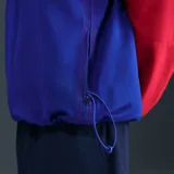 Campera deportiva Nike del Paris Saint-Germain, modelo Total 90 Reissue 2004, de color azul con una de las mangas en color rojo. Cuenta con cierre frontal completo, cuello alto y bolsillos laterales.