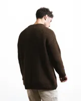 Buzo unisex de tejido de punto grueso en lana merino, color rojo, con cuello redondo y diseño de calce relajado. Presenta un detalle bordado a mano en contraste en la manga.