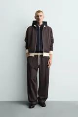 Pantalón jogger de corte wide fit en tejido compacto color gris oscuro. Presenta cintura elástica con cordón ajustable, bandas laterales en contraste color beige y costuras frontales tipo pinza.