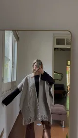 Ruana tejida a mano en lana merino, color gris, con diseño de textura en la parte inferior y terminación con flecos.