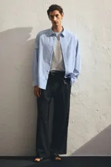 Camisa celeste y blanca a rayas verticales, de corte holgado, manga larga, cuello inglés, bolsillo en el pecho y cierre con botones.