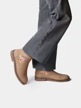 Botin de cuero serraje color beige, con elastico lateral decorado con bordado floral multicolor y suela baja de goma.