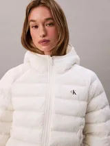 Campera puffer ligera Calvin Klein de color blanco, con diseño acolchado horizontal, capucha integrada y cierre frontal con cremallera. Presenta el logo de la marca bordado en el pecho.