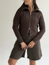 Sweater tipo campera de tejido de punto con diseño de trenzas, color blanco, con cuello alto y cierre frontal completo.