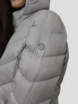 Campera puffer color beige con capucha, cierre frontal con cremallera y bolsillos laterales. Relleno de plumón (90% plumón, 10% plumas).