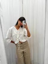 Blusa negra de lino con acabado brillante, de manga larga abullonada, escote con volados y cierre frontal con tiras para anudar.