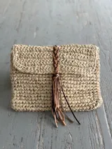Sobre de rafia color beige con cierre tipo sobre y detalle de tira de cuero trenzado con flecos.