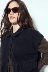 Chaleco de jean con corte oversized, diseño sin mangas, cuello camisero, cierre frontal con botones metálicos y bolsillos frontales tipo cargo.