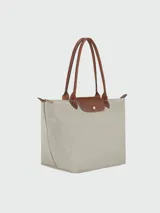 Bolso tipo tote de la línea Le Pliage Original de Longchamp, confeccionado en nylon color beige con detalles en cuero marrón, incluyendo asas largas y solapa frontal con cierre de botón a presión.