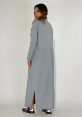 Vestido largo tipo camisero color beige, con botones frontales, cuello camisero, mangas largas con puños abotonados y bolsillos en el pecho.