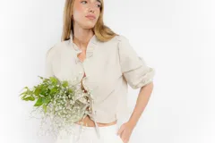 Blusa corta blanca de lino con mangas 3/4 abullonadas, escote en V con volados y cierre con lazos.