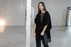 Ruana negra de tejido de punto con diseño abierto, terminación con flecos en el ruedo y corte holgado.