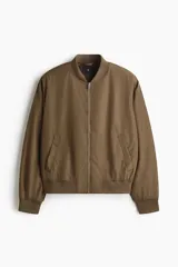 Campera bomber liviana H&M de color verde militar, con cuello, puños y dobladillo acanalados. Cuenta con cierre frontal plateado, bolsillos laterales con solapa y diseño clásico de aviador.