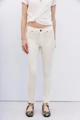 Jean tiro alto, calce skinny, color blanco, con acabado símil cuero y pierna ajustada hasta el tobillo.