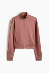 Campera deportiva corta de punto grueso con leve brillo, color rosado, con cuello elevado, cierre frontal y bolsillos laterales insertados.