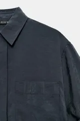 Camisa de corte fluido confeccionada en mezcla de modal, con cuello solapa, manga corta con dobladillo y bolsillo de plastrón en el delantero. Presenta cierre frontal con botones ocultos por tapeta y aberturas laterales en el bajo.
