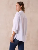 Camisa blanca de lino con cuello con solapa, manga larga regulable con presilla y botón, y abertura central con botones.