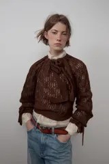Jersey de punto calado color marrón, con cuello redondo ajustable mediante lazada y mangas largas con puños ajustables con lazos.