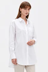 Camisa blanca de algodón, de corte holgado y largo tipo túnica, con cuello camisero, cierre frontal con botones y un bolsillo aplicado en el pecho.