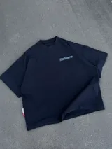 Remera negra oversize de manga corta, con estampa tipográfica vertical en la espalda y logo pequeño en el frente.