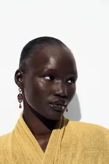 Pendientes de aro dorados con colgante en forma de calavera esmaltada con detalles florales en rojo y azul. Cuelga una joya engarzada con forma de gota de color rosa/fucsia.