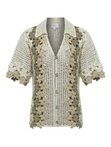 Sweater tejido a crochet color crema con flores bordadas en tonos beige y marrón. Tiene cuello camisero, mangas cortas y cierre frontal con botones.