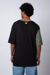 Remera de corte oversize en color beige, con cuello redondo en contraste negro y una manga en color negro. Presenta un pequeño estampado circular en el pecho con la frase 'Don't worry, be happy'.