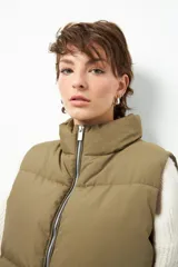 Chaleco puffer color beige, sin mangas, con cuello alto y cierre frontal con cremallera.
