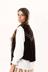 Chaleco oversize confeccionado en cuero descarne, con diseño de terminación en picos. Presenta lazos frontales con ojalillos metálicos y detalle de tachas metálicas en hombros y espalda.