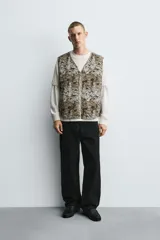 Chaleco acolchado de algodón con cuello pico y cierre frontal de cremallera. Presenta un estampado abstracto en tonos tierra y gris, con bolsillos de vivo en la cadera.