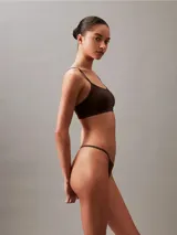 Bombacha tipo colaless Calvin Klein de la línea Ideal Cotton, confeccionada en mezcla de algodón y elastano. Presenta un diseño de talle medio con laterales y parte trasera estilo cuerda, y cuenta con una cinturilla elástica con el logo de la marca.