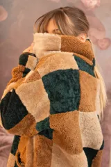 Buzo de cuero de oveja con diseño de parches cuadrados en tonos marrón, beige y verde oscuro. Presenta cuello alto con interior de piel sintética y cierre frontal.