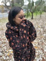 Buzo color beige de poliéster con textura de piel de oso, capucha con cuello alto, mangas largas y bolsillo tipo canguro.