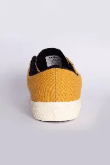 Zapatillas casuales color mostaza con cordones negros y suela blanca.