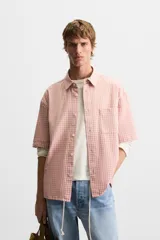Camisa de corte relajado confeccionada en algodón, con estampado de cuadros pequeños en tonos rosados. Presenta cuello solapa, manga corta y bolsillo plastrón en el pecho con cierre frontal de botones.